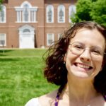 A photo of Mia smiling outside of a building that looks like its from a university campus