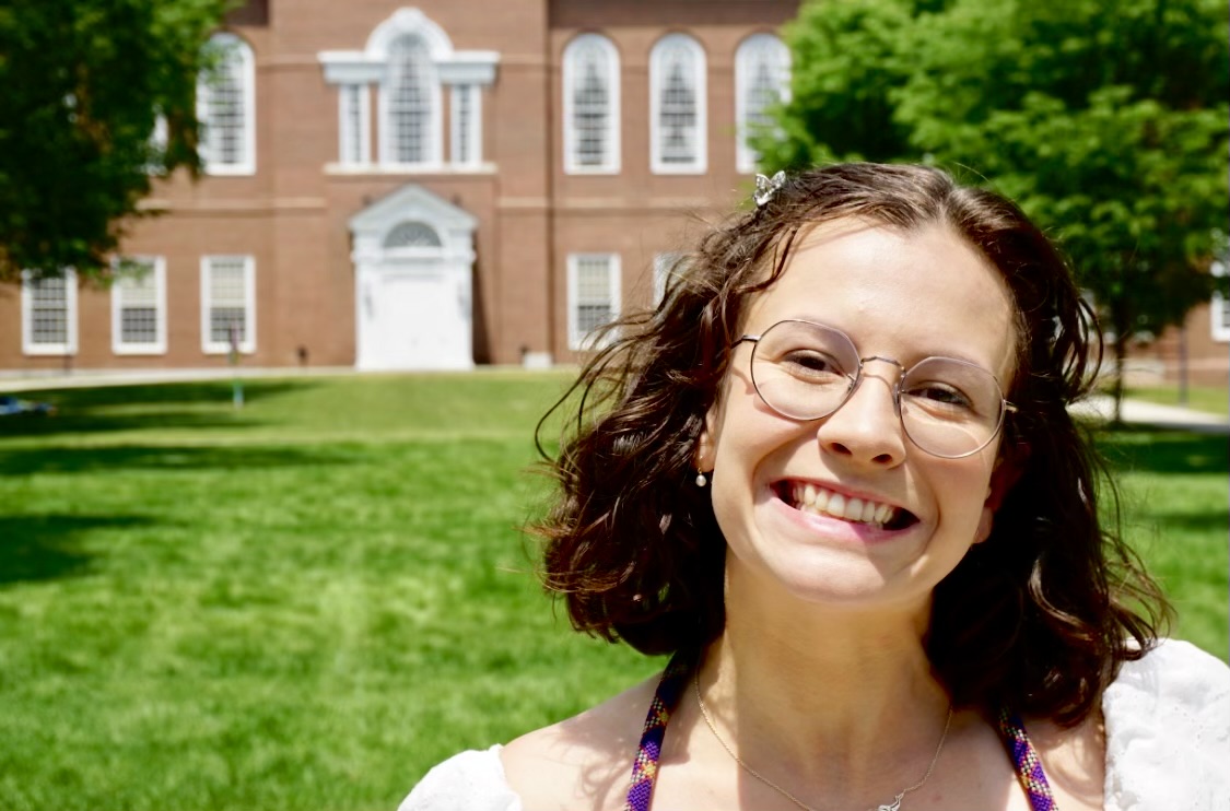 A photo of Mia smiling outside of a building that looks like its from a university campus