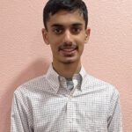 A headshot of Arnav in a white shirt in front of a pink wall.