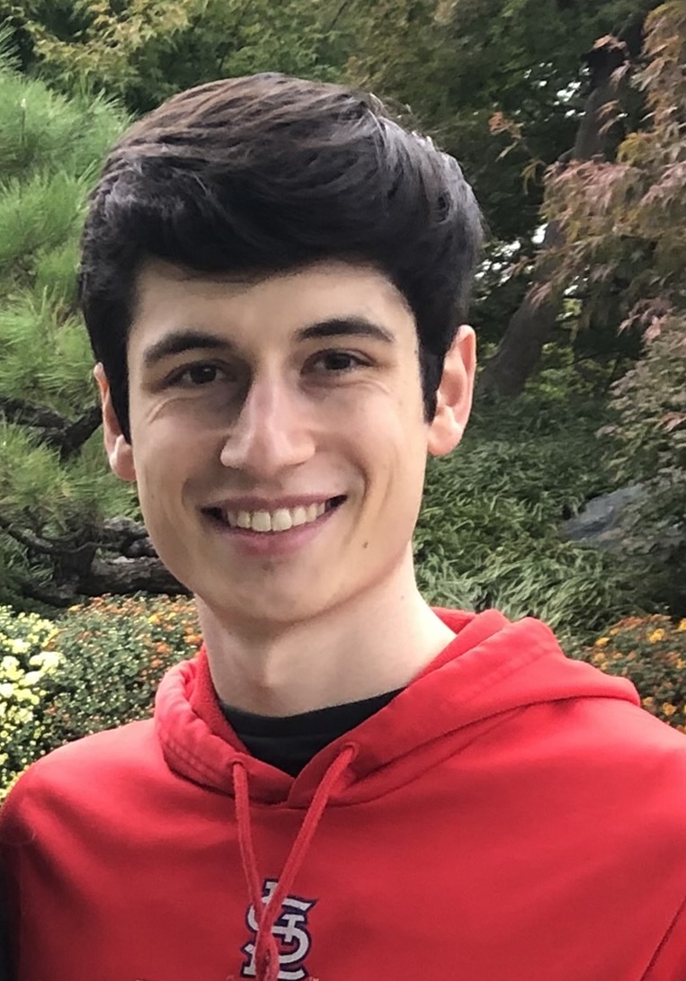 Photo of Rafeal in a red hooded sweatshirt standing in front of a tree.