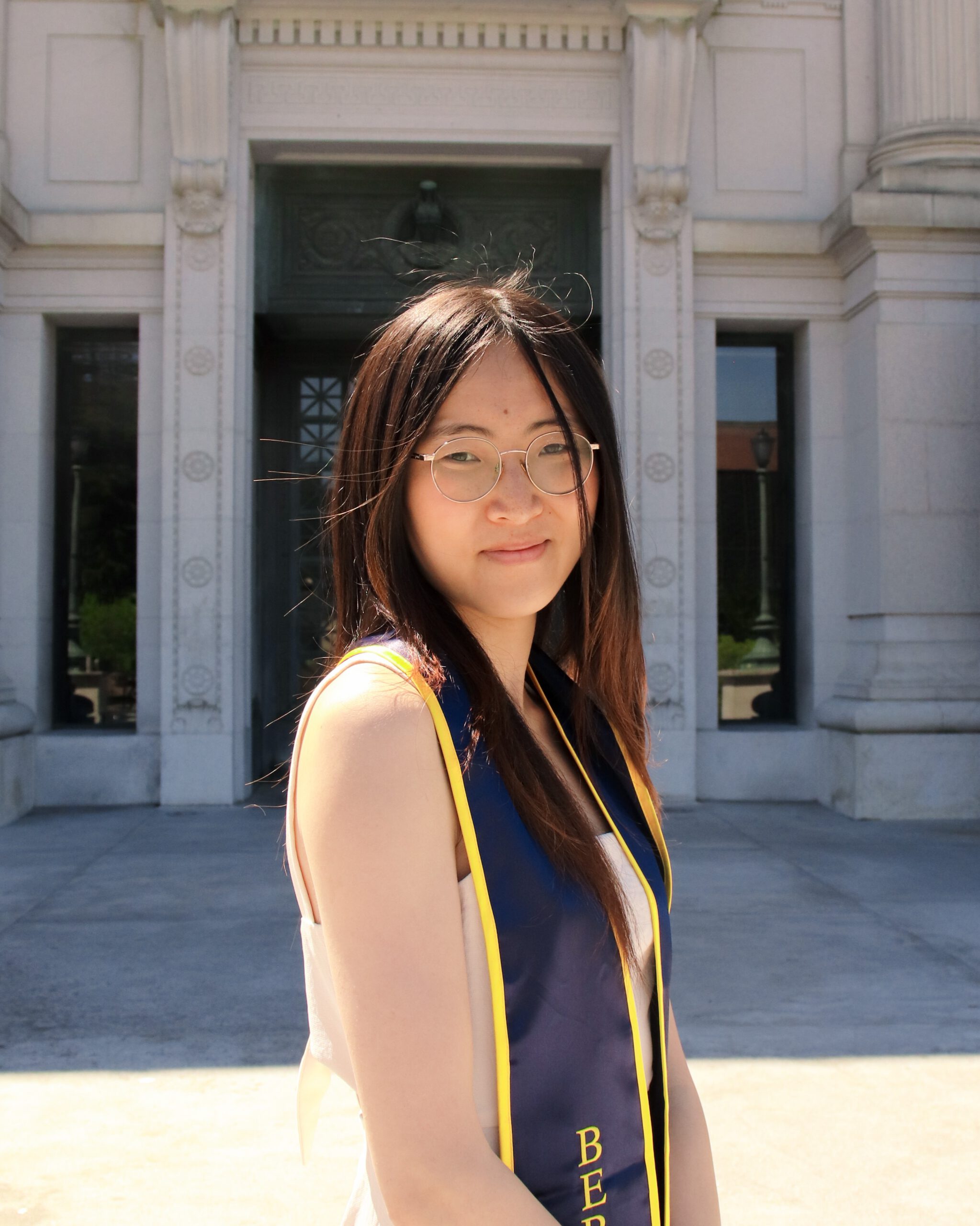 Avery standing outside of a building in a dress and graduation sash